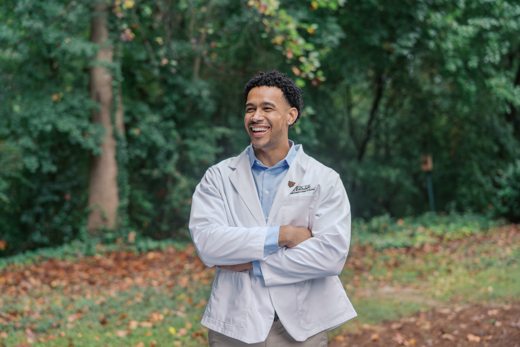 A nursing student in a white coat stands outside.